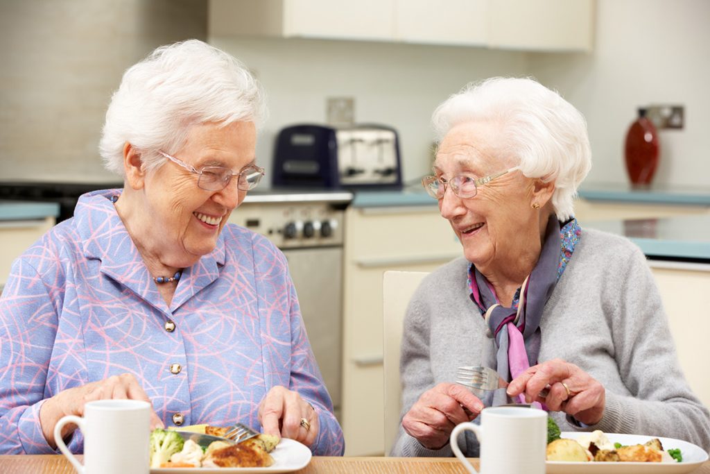 Two joyful elderly ladies sharing a lighthearted moment, laughing warmly in the comfortable surroundings of a Modesto assisted living facility. Their genuine smiles reflect the sense of companionship and happiness found in the community.