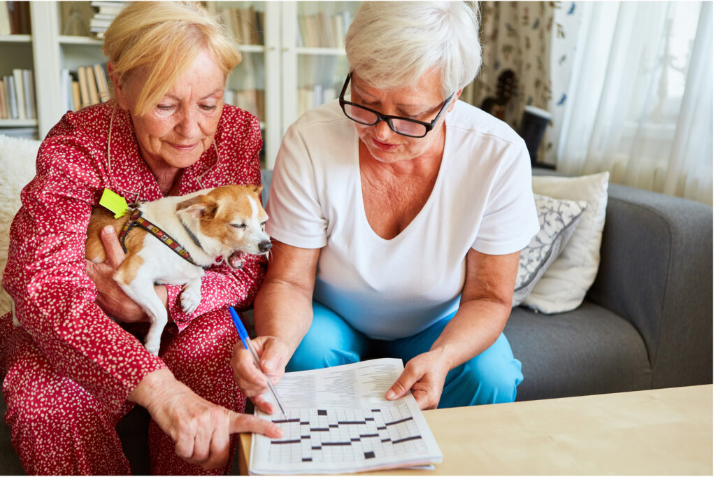 Two elderly women sitting together, engrossed in reading a newspaper, while tenderly cradling a small dog in their arms during a beautiful afternoon in an assisted living facility located in Modesto
