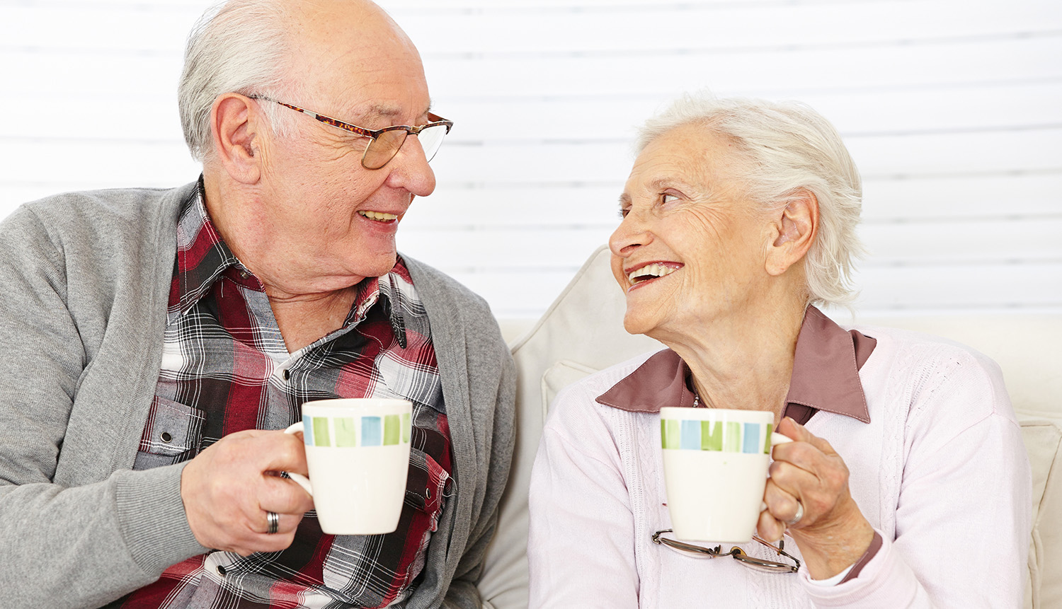 elderly couple laughing over a cup of coffee, while researching resources for senior care