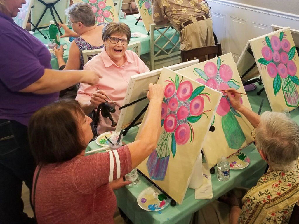 elderly lady is smiling as she is painting during a workshop at Graceful Living in Oakdale.