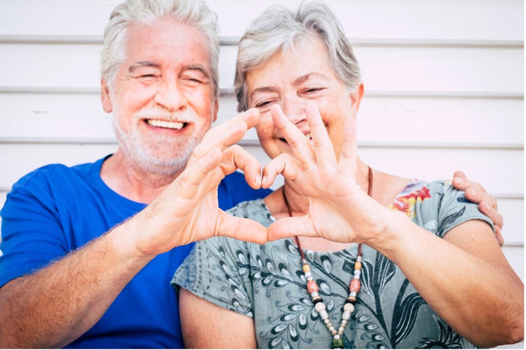 two elderly people smiling making the heart sign