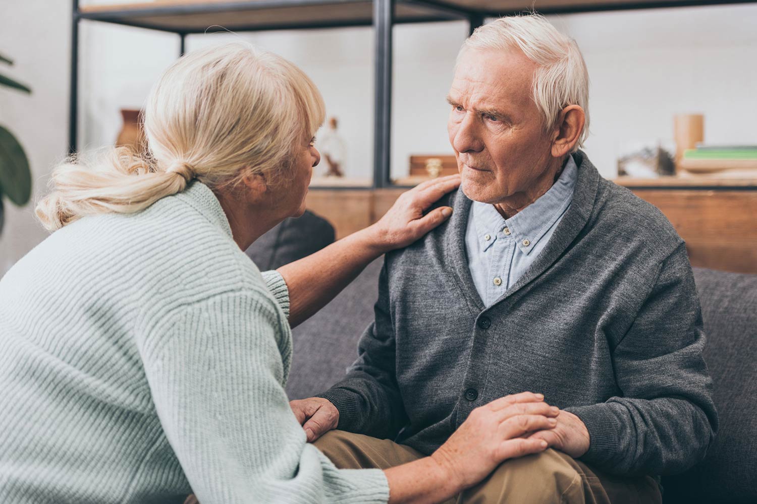 "Two elderly residents in a cozy care home in Modesto, sitting together on a sofa, smiling and enjoying a peaceful afternoon in a warm, home-like environment."