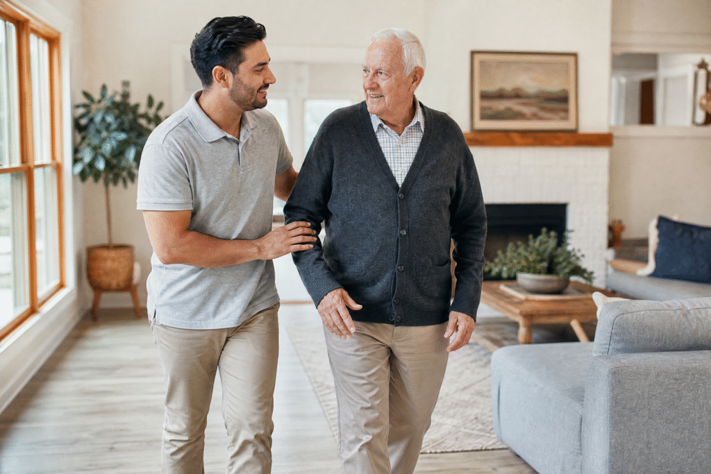Caregiver walking beside an older man in a comfortable residential living room